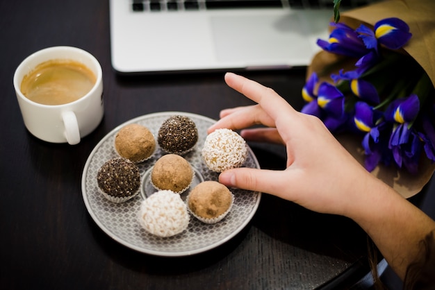 Foto gratuita primer plano de la mano que sostiene trufas surtidas gourmet de la placa en el escritorio negro