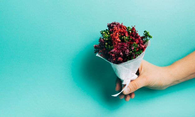 Primer plano de la mano con ramo de flores decorativas sobre fondo turquesa