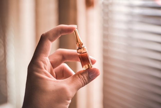 Primer plano de una mano sosteniendo una ampolla bajo la luz del sol con una ventana