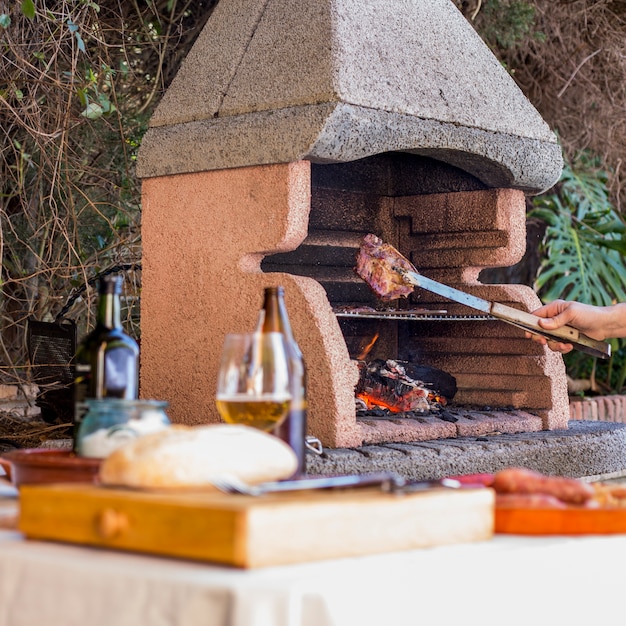 Primer plano de mano sosteniendo carne a la parrilla con pinzas en barbacoa al aire libre