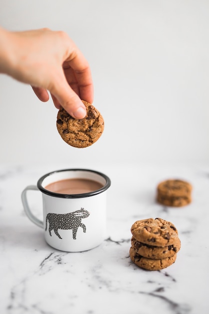 Primer plano de mano sosteniendo la cookie sobre la taza de té en el fondo de mármol