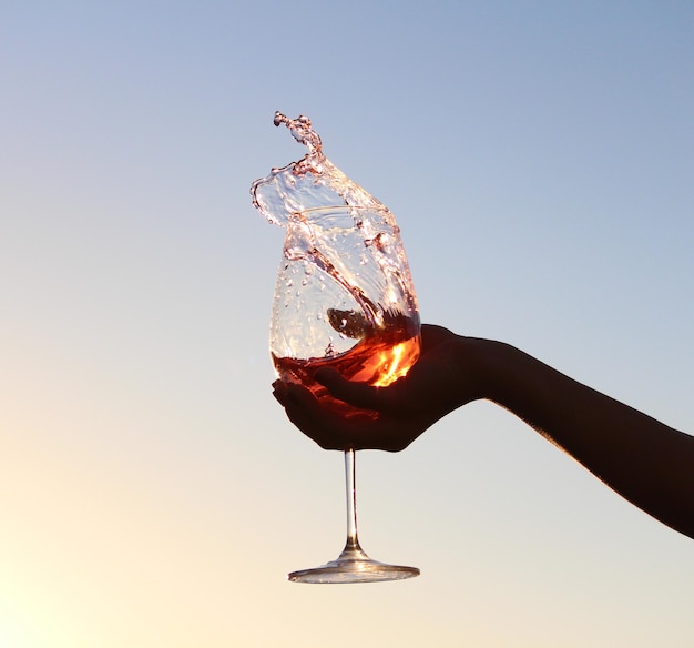 Primer plano de una mano sosteniendo una copa de vino salpicada