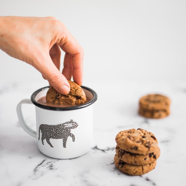 Foto gratuita primer plano de mano sumerge cookie en taza de café sobre fondo de mármol