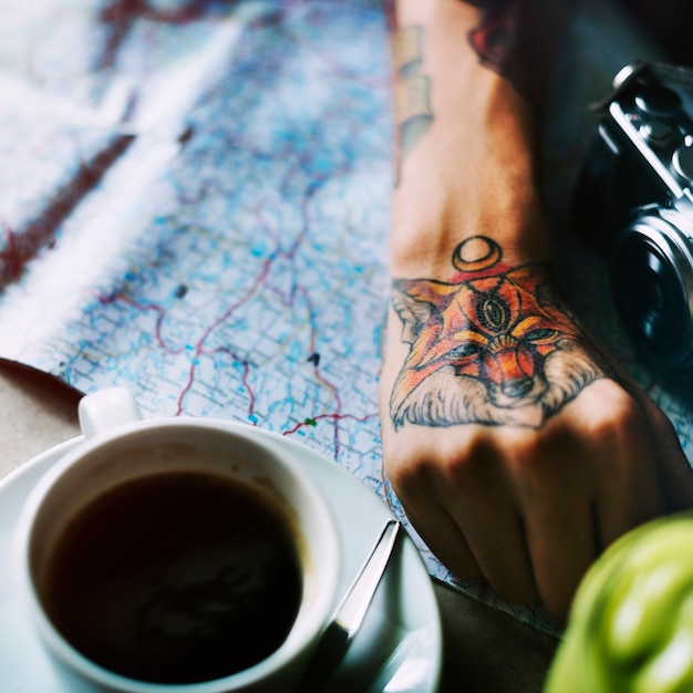 Primer plano de la mano del tatuaje con el mapa y la taza de café