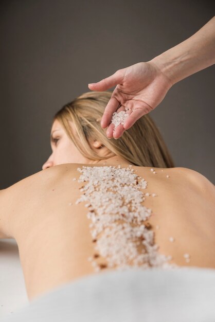 Primer plano de una mano de terapeuta aplicando sal en la espalda de la mujer