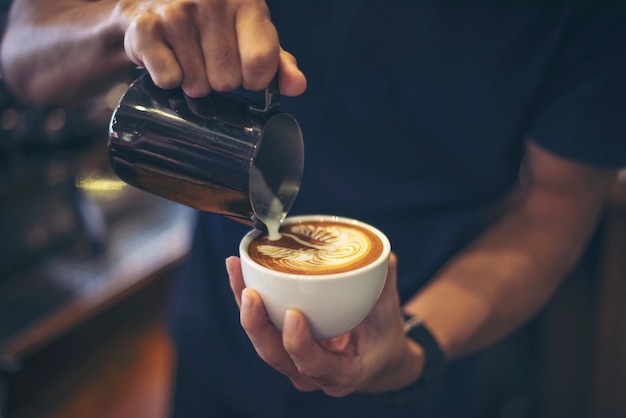 Primer plano de manos barista hacer café con leche arte pintura