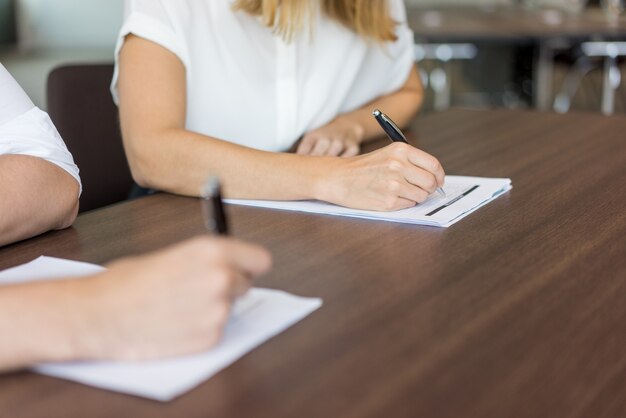 Primer plano de las manos de los estudiantes escribir el examen en los papeles.