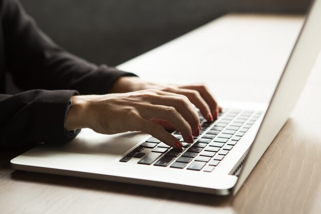 Primer plano de las manos femeninas escribiendo en la computadora portátil en la mesa