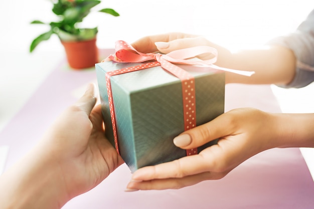 Primer plano de manos femeninas con un presente. Escritorio rosa de moda.