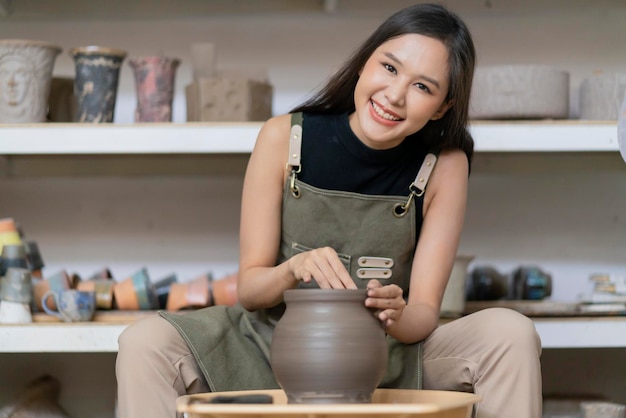 Primer plano de las manos femeninas que trabajan en alfareros rueda escultura femenina asiática mujer formando molde pequeño jarrón tazón de arcilla en la rueda de alfarero en casa estudio taller arte y creación hobby concepto