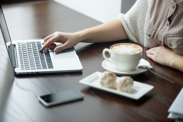 Primer plano de las manos femeninas que trabajan en la computadora portátil en el café