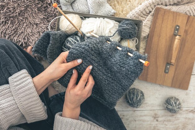 Primer plano de manos femeninas tejiendo un suéter de lana gris vista superior