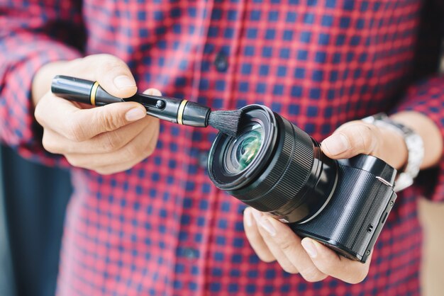 Primer plano de las manos de un fotógrafo profesional limpiando el polvo de la lente de la cámara con un cepillo