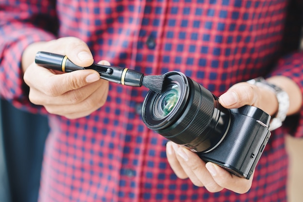 Primer plano de las manos de un fotógrafo profesional limpiando el polvo de la lente de la cámara con un cepillo