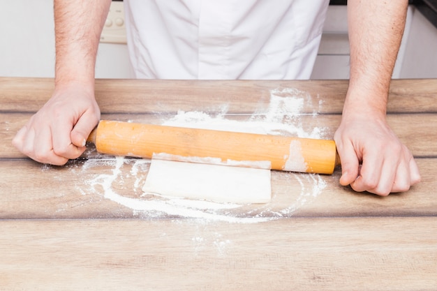 Foto gratuita primer plano de las manos de un hombre que desarrollan la masa en la mesa de la cocina