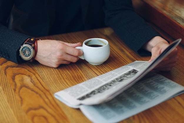 Primer plano de las manos del hombre sosteniendo una taza de café y un periódico