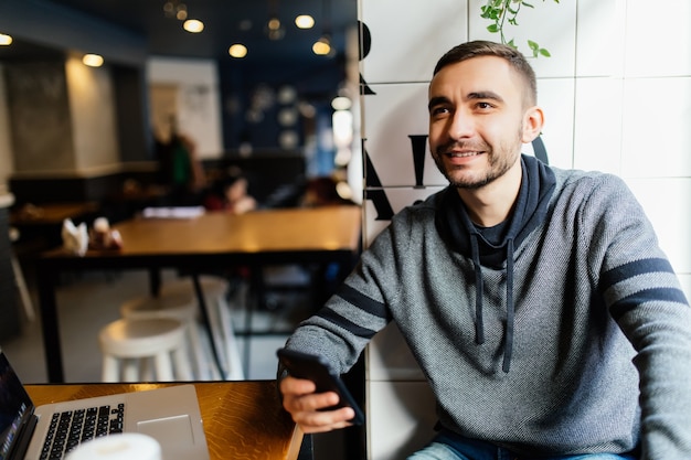 Primer plano de manos masculinas sosteniendo y usando un teléfono inteligente moderno en la cafetería.