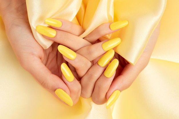 Primer plano de las manos de una mujer con esmalte de uñas amarillo sobre una tela de seda amarilla
