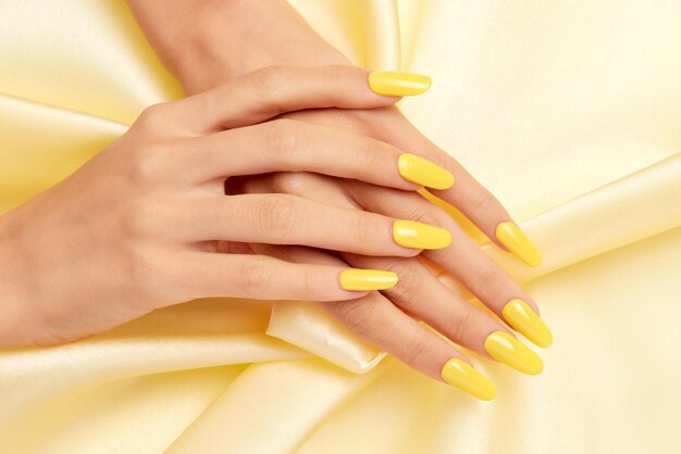 Primer plano de las manos de una mujer con esmalte de uñas amarillo sobre una tela de seda amarilla