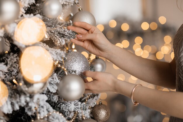 Primer plano de las manos de la mujer tierna poniendo un juguete de plata en el árbol de Navidad