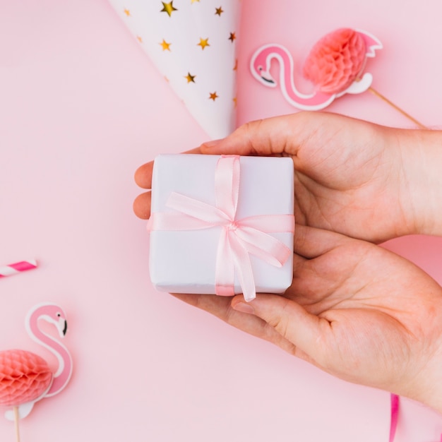 Primer plano de manos que muestran una caja de regalo envuelta en blanco atada con una cinta rosa