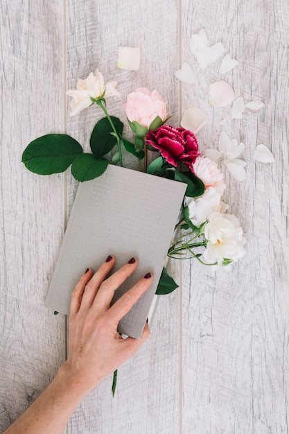 Primer plano de manos sosteniendo diario con flores en la mesa de madera