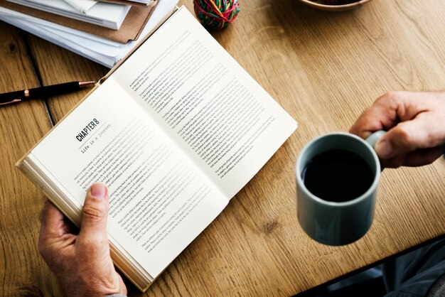 Primer plano de manos sosteniendo una taza de café y novela abierta