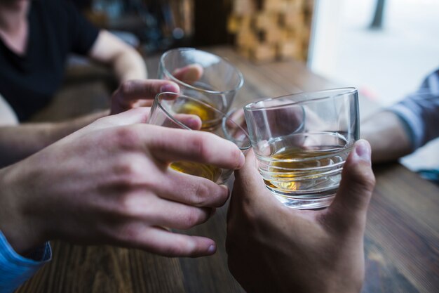 Primer plano de manos tostando vasos de whisky