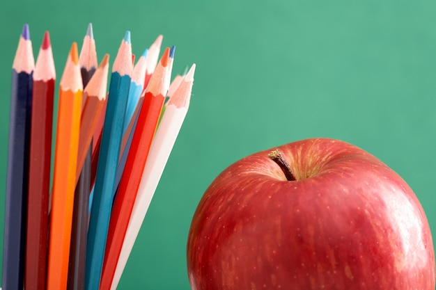 Primer plano de una manzana y lápices con la pizarra de fondo