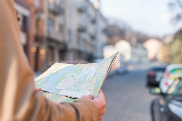 Foto gratuita primer plano del mapa de la tenencia del viajero masculino en la mano que se coloca en la calle de la ciudad