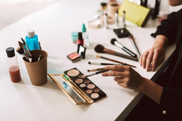 Primer plano maquillador sentado en el escritorio con una variedad de productos cosméticos aislados