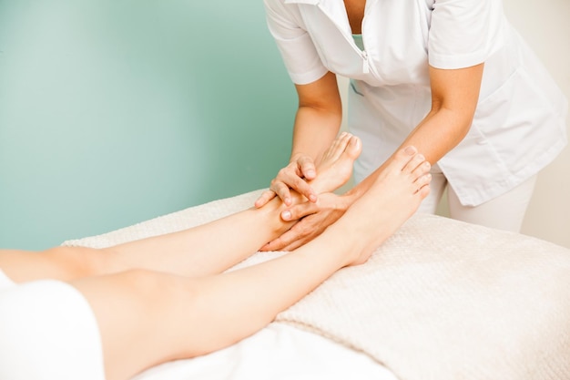 Primer plano de una masajista femenina dando un masaje de pies a uno o sus clientes en un spa de salud y belleza