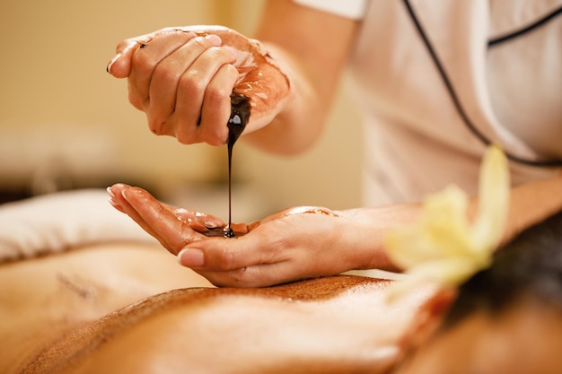 Primer plano de masajista vertiendo chocolate caliente en sus manos antes del tratamiento de spa