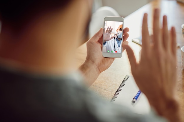 Primer plano de un médico afroamericano saludando a su paciente durante una videollamada por teléfono móvil