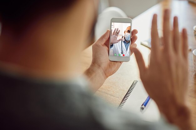 Primer plano de un médico afroamericano saludando a su paciente durante una videollamada por teléfono móvil