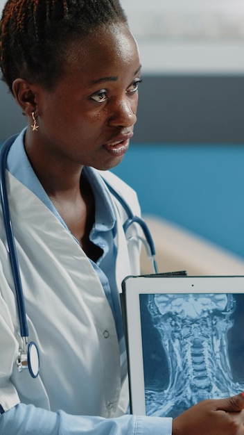 Primer plano del médico que apunta a la pantalla de la tableta con radiografía, analizando la estructura ósea y el diagnóstico de atención médica en el gabinete. Doctor sosteniendo un aparato moderno con escaneo de rayos x en la pantalla.