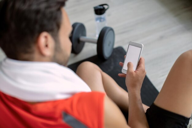 Primer plano de mensajes de texto de deportista en el teléfono móvil en un gimnasio