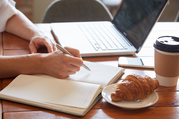 Primer plano de la mesa de desayuno con manos femeninas que ponen información al planificador diario