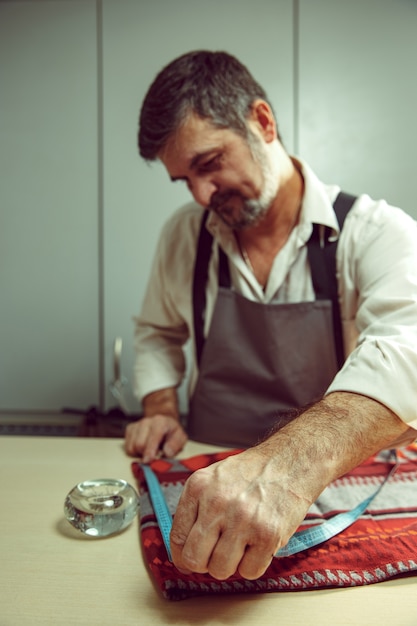 Primer plano de la mesa de sastres con manos masculinas trazando patrón de fabricación de tela para ropa en el estudio de taller tradicional. El hombre de profesión femenina. Concepto de igualdad de género