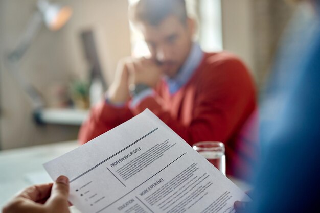 Primer plano de un miembro de recursos humanos verde azulado leyendo el CV del candidato durante la reunión en la oficina