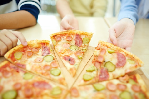 Primer plano de los muchachos cogiendo la pizza caliente