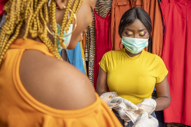 Primer plano de una mujer africana con guantes de látex y una mascarilla pagando con efectivo en una tienda