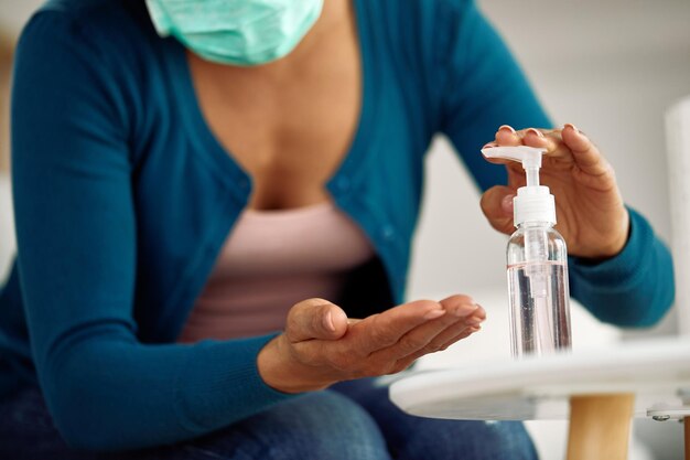 Primer plano de una mujer afroamericana limpiándose las manos con gel antibacteriano en casa
