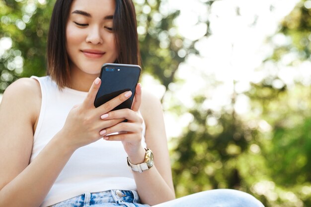 Primer plano de mujer asiática joven con teléfono móvil mientras está sentado en el parque