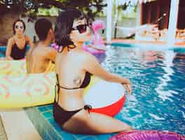 Foto gratuita primer plano de mujer asiática sentada junto a la piscina con amigos diversos