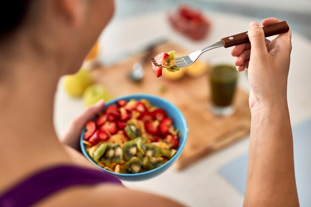 Primer plano de mujer atlética comiendo ensalada de fruta fresca en la cocina