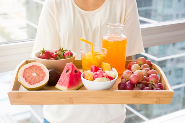 Primer plano de una mujer con bandeja de madera de varias frutas