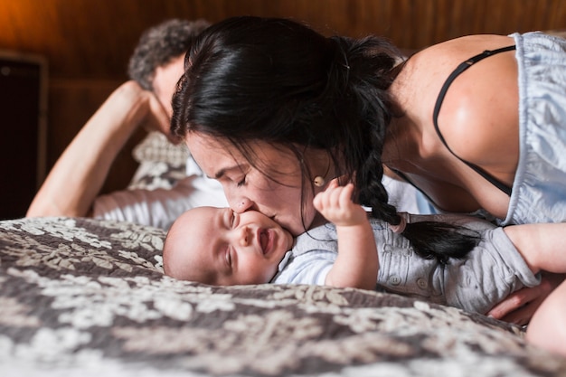 Primer plano de mujer besando a su bebé acostado en una cama acogedora