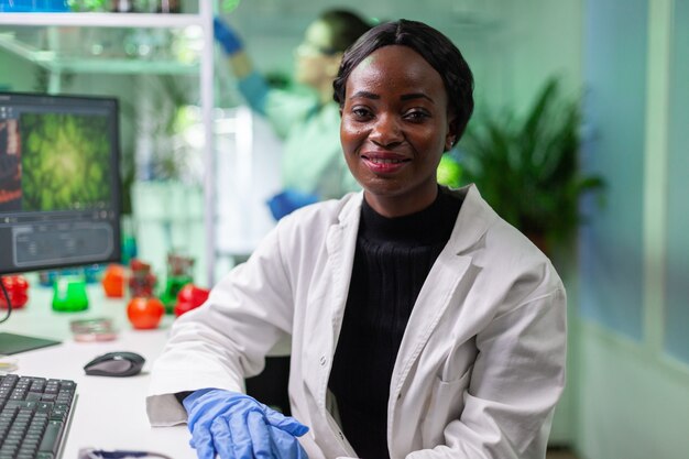 Primer plano de una mujer bióloga africana mirando a la cámara mientras trabajaba en el laboratorio biológico