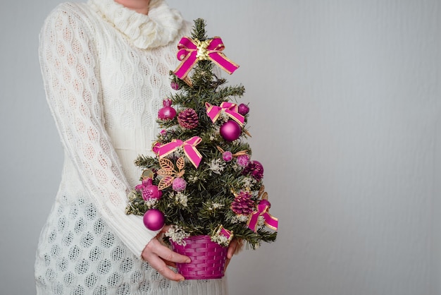 Primer plano de una mujer blanca sosteniendo un pequeño árbol de Navidad en una olla con adornos de color púrpura